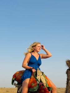 Best Desert Camp In Jaisalmer Red Velvet في جيلسامر: امرأة ترتدي ثوب أزرق تجلس على خيل