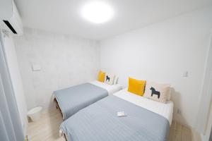 two beds in a white room with yellow pillows at Family Home Petit Denpo 101 in Osaka