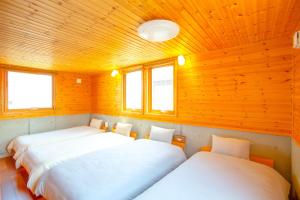 two beds in a room with wooden walls and windows at 「KIRAKU」Wood House稚内 in Wakkanai
