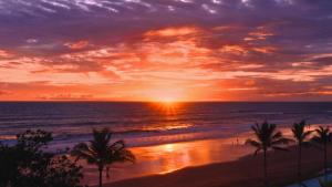 a sunset over a beach with palm trees and the ocean at Potato Head Suites & Studios in Seminyak