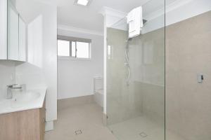 Un baño blanco con ducha y lavabo. en The Entrance Hideaway, en The Entrance 2 fotos más