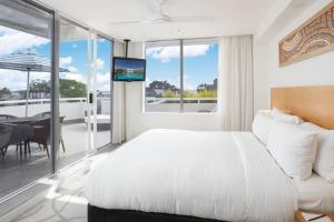 a bedroom with a bed and a balcony with a table at Sofitel Noosa Pacific Resort in Noosa Heads