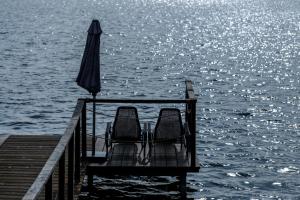 zwei Stühle auf einem Dock mit Regenschirm und Wasser in der Unterkunft Argo Trakai in Trakai