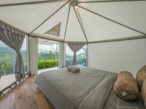 ein Schlafzimmer mit einem Bett und einem großen Fenster in der Unterkunft Alam Kita Glamping & Plantation in Munduk