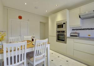 a kitchen with white chairs and a table and a stove at Hen Ysgol in Beaumaris