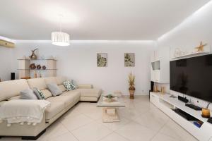 sala de estar blanca con sofá y TV en Zurrinha holidays, en Quarteira