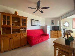 un sofá rojo en la sala de estar con ventilador de techo en Sol-y-Days Californie, Appartement confortable 4 personnes à 300m de la plage, en Le Grau-du-Roi