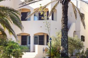 a building with black shutters and a palm tree at Apartamentos Verde Mar in Es Pujols