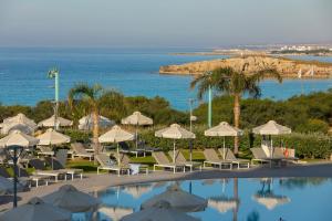 a pool with chairs and umbrellas next to the ocean at NissiBlu Beach Resort in Ayia Napa