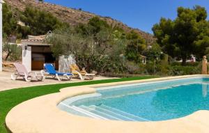 a swimming pool with two blue chairs and a house at Chalet Los Olivos con piscina in Jávea