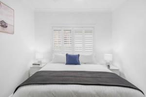 a white bedroom with a large bed with a blue pillow at Marlo's Escape - A Generous Haven for Couples in Wollongong