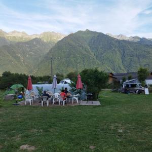 um grupo de pessoas sentadas em mesas em um campo com montanhas em Maurienne Outdoor - Nuit insolite en Yourte en Savoie em Saint-Georges-des-Hurtières