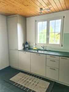a kitchen with white cabinets and a sink and two windows at Abendberg - zentral nähe Bahnhof in Wilderswil