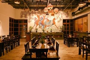 a dining room with tables and chairs and a large mural at Saj In The Forest, Pench National Park in Seonī