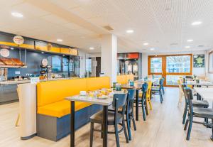 un restaurante con mesas y sillas y un banco amarillo en B&B HOTEL Poitiers 3 Futuroscope en Chasseneuil-du-Poitou