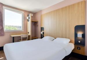 Un dormitorio con una gran cama blanca y una ventana en B&B HOTEL Béziers en Béziers