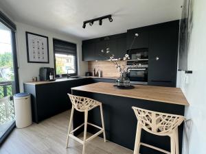 une cuisine avec des placards noirs et un comptoir avec deux tabourets dans l'établissement Duplex 100m2 style contemporain, à Seraing