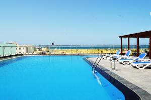 a swimming pool with lounge chairs and the beach at Sur Grand Hotel in Sur