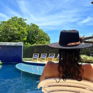 a woman in a hat sitting in a chair next to a swimming pool at Pousada Solar Dos Carneiros in Praia dos Carneiros