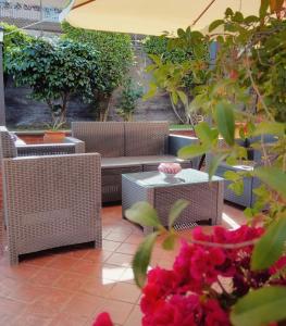 a patio with wicker chairs and tables and pink flowers at Villa Hirschen in Zafferana Etnea