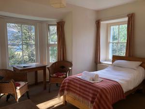 een slaapkamer met een bed, een bureau en ramen bij Trigonos - Peaceful Lakeside Vegetarian B&B and Retreat in Eryri National Park in Caernarfon