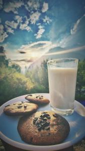 two cookies on a plate with a glass of milk at Old Brahma Homestay in Kalgha