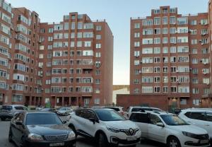 a parking lot with cars parked in front of tall buildings at 1 комнатные апартаменты in Pavlodar