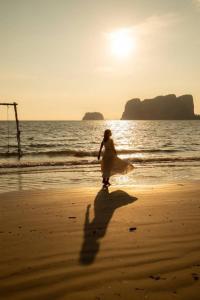 Una donna che cammina sulla spiaggia al tramonto di Modtanoi Paradise Homestay a Ban Bu Lu