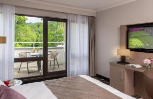 a hotel room with a television and a balcony at Leonardo Royal Hotel Baden- Baden in Baden-Baden