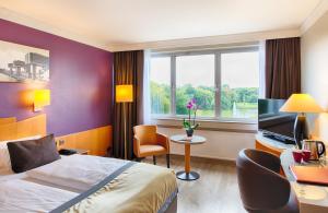 ein Hotelzimmer mit einem Bett, einem Schreibtisch und einem TV in der Unterkunft Leonardo Royal Hotel Köln - Am Stadtwald in Köln
