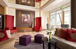 a living room with a couch and red chairs at Leonardo Hotel Aachen in Aachen