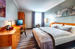 a hotel room with a bed and a desk and a television at Leonardo Hotel Aachen in Aachen