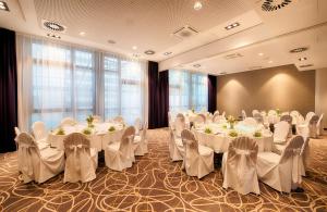 um salão de banquetes com mesas e cadeiras brancas em Leonardo Hotel Wolfsburg City Center em Wolfsburg