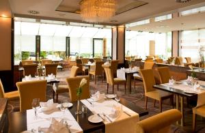 een restaurant met tafels, stoelen en ramen bij Leonardo Hotel Köln Bonn Airport in Keulen
