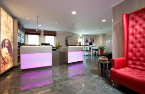 a living room with a red chair and a kitchen at Leonardo Hotel Nürnberg in Nuremberg