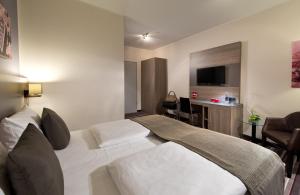 a hotel room with a white bed and a desk at Leonardo Hotel Nürnberg in Nuremberg