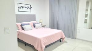 a white bedroom with a pink bed with blue pillows at Opera Villa Carlos Paz in Villa Carlos Paz