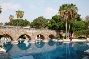 an old stone bridge over a swimming pool with palm trees at Hotel Hacienda Vista Hermosa in Tequesquitengo