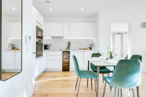 a white kitchen with a table and green chairs at Pluxa Emerald Luxury - Walk to Attractions, Transport Nearby in Birmingham