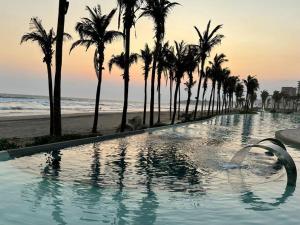 a swimming pool next to a beach with palm trees at Luxurious First-Floor Apartment in Isla Residences in Acapulco