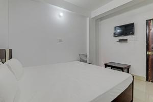OYO Hotel R Glory في باتنا: غرفة نوم بيضاء مع سرير وتلفزيون على الحائط