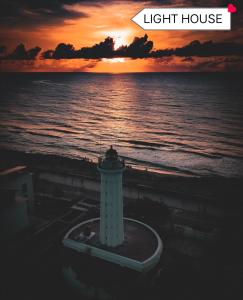 ein Leuchtturm am Strand mit Sonnenuntergang im Hintergrund in der Unterkunft The Elite Beachview in Puducherry