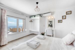 a white bedroom with a bed and a large window at Dream Villa Santorini in Vourvoulos