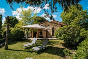 a stone house with two chairs and an umbrella at Borgo Il Poggiaccio Residenza d'Epoca in Sovicille