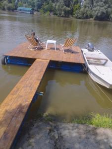 a dock with chairs and a boat on the water at Vikendica DUNAV in Novi Sad