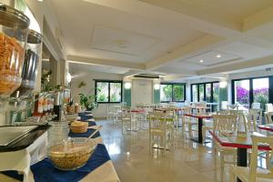 restauracja z białymi krzesłami, stołami i oknami w obiekcie Hotel & Apartments Villa Linda w mieście Giardini Naxos