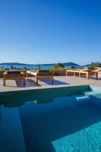 a swimming pool with benches and the ocean in the background at Gialova Hills Luxury Villas with Private Pool in Gialova