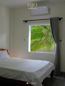 a bedroom with a bed and a window with a palm tree at Gạo Homestay in Mui Ne