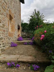 La Vieille Ferme في Donnay: حديقة بها زهور أرجوانية بجوار مبنى حجري