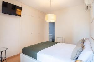 um quarto com uma cama branca e uma televisão na parede em R&B MUNTANER em Barcelona